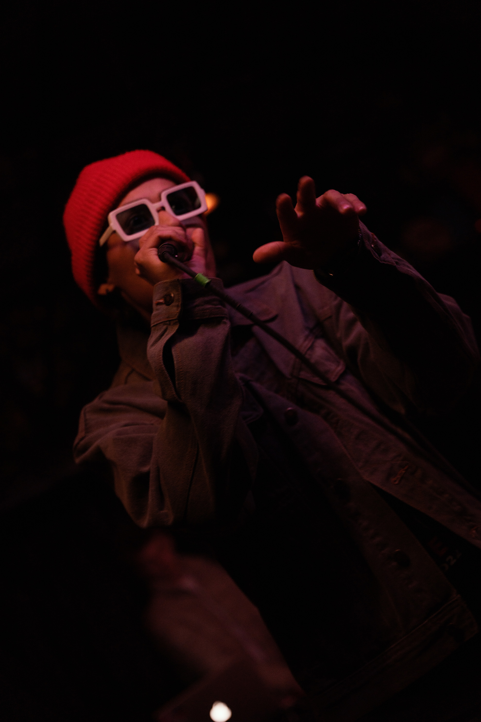 Rapper in a orange beanie and white sunglasses, rapping to the crowd