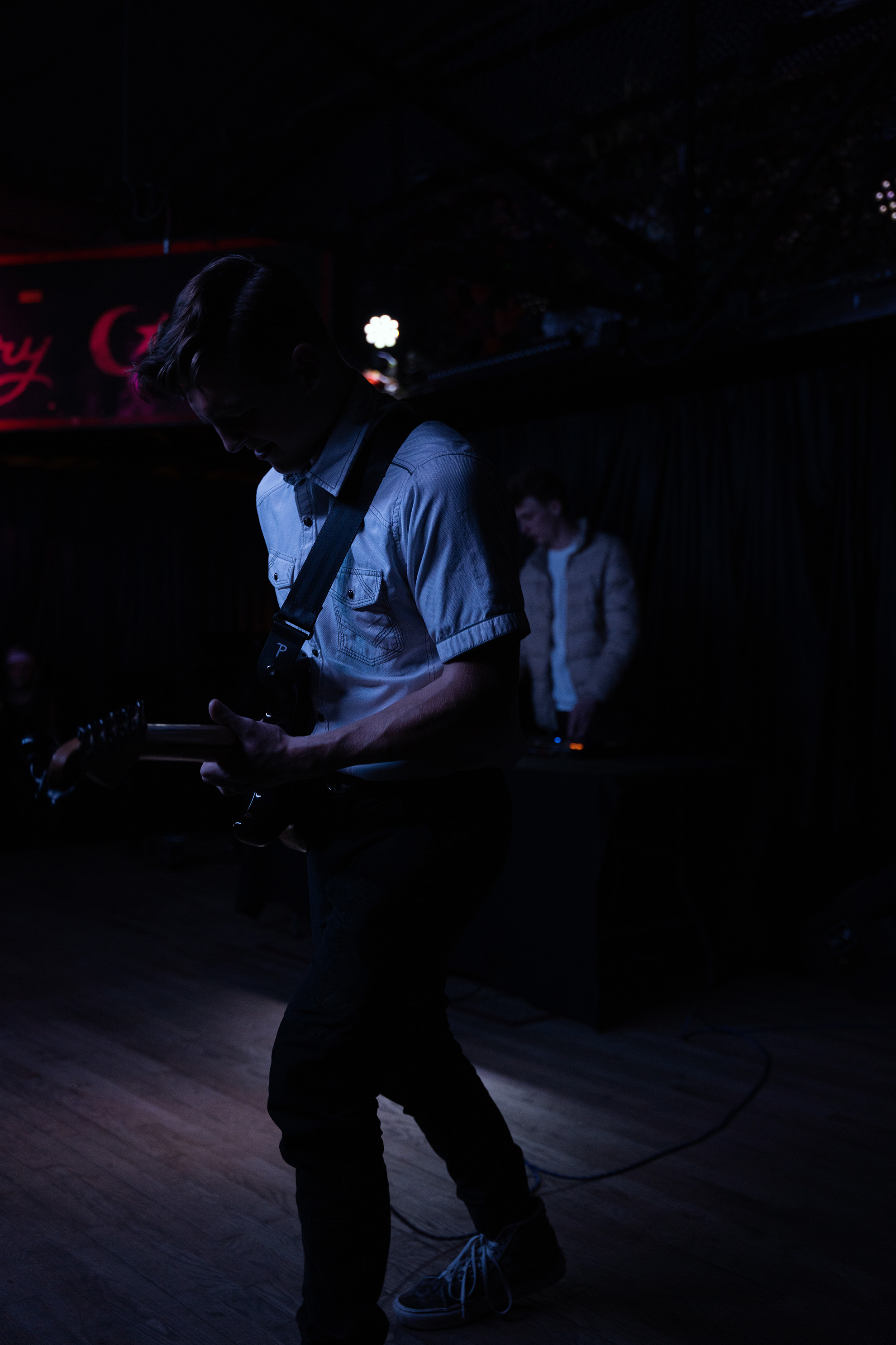 Guitar player in a blue lighting with a dj in the background